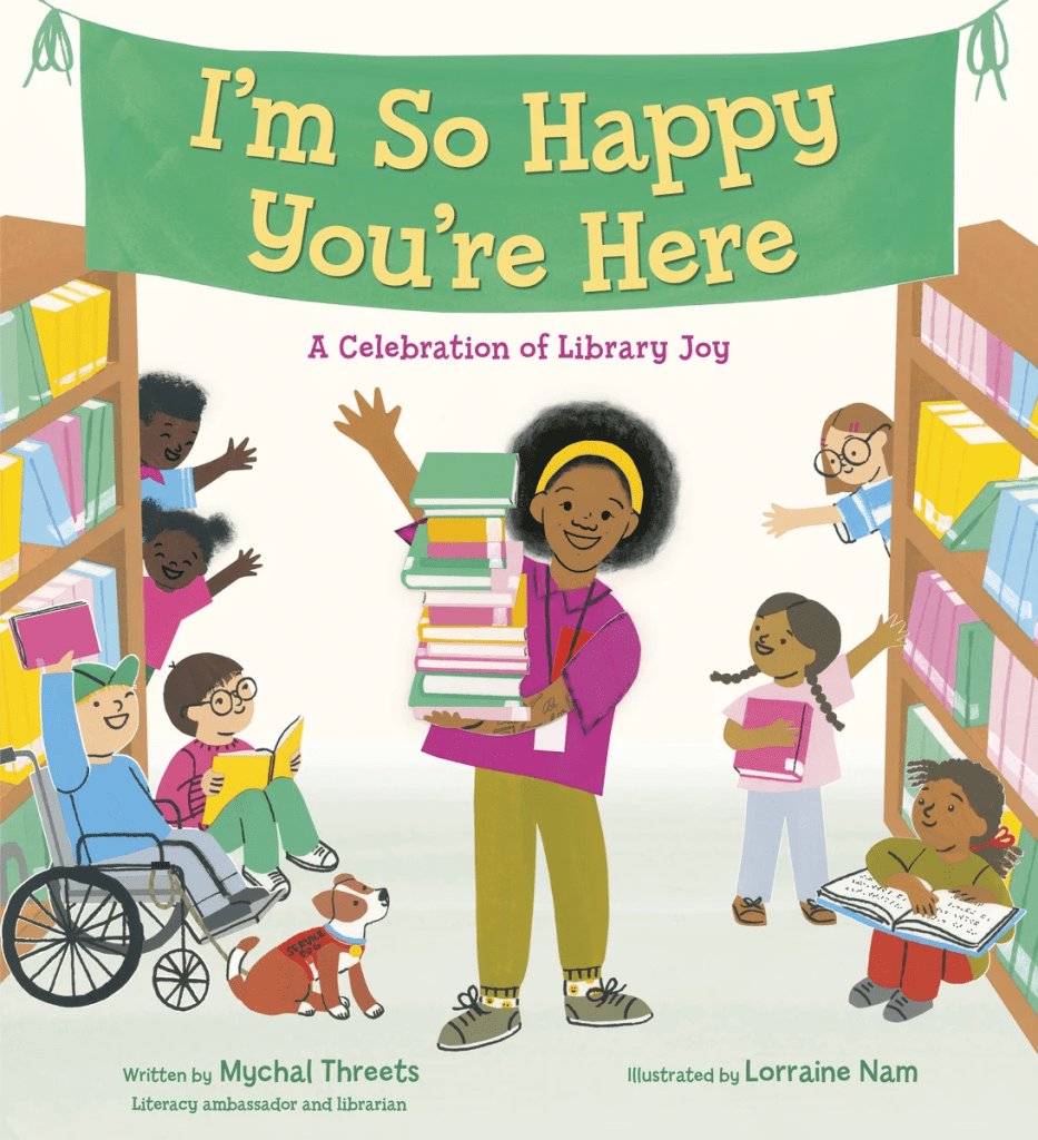 Cover image for I’m So Happy You’re Here: A Celebration of Library Joy by Mychal Threets, illustrated by Lorraine Nam. Features Mychal Threets in the middle of the page standing in a library, holding a pile of books and waving. Children are around him using the library as well as a small dog.